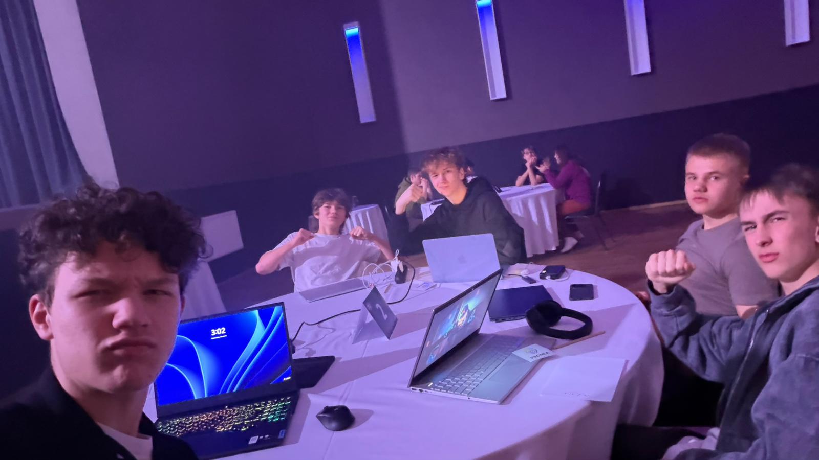 The team at their table with laptops late at night, a laptop clock reading 3:02