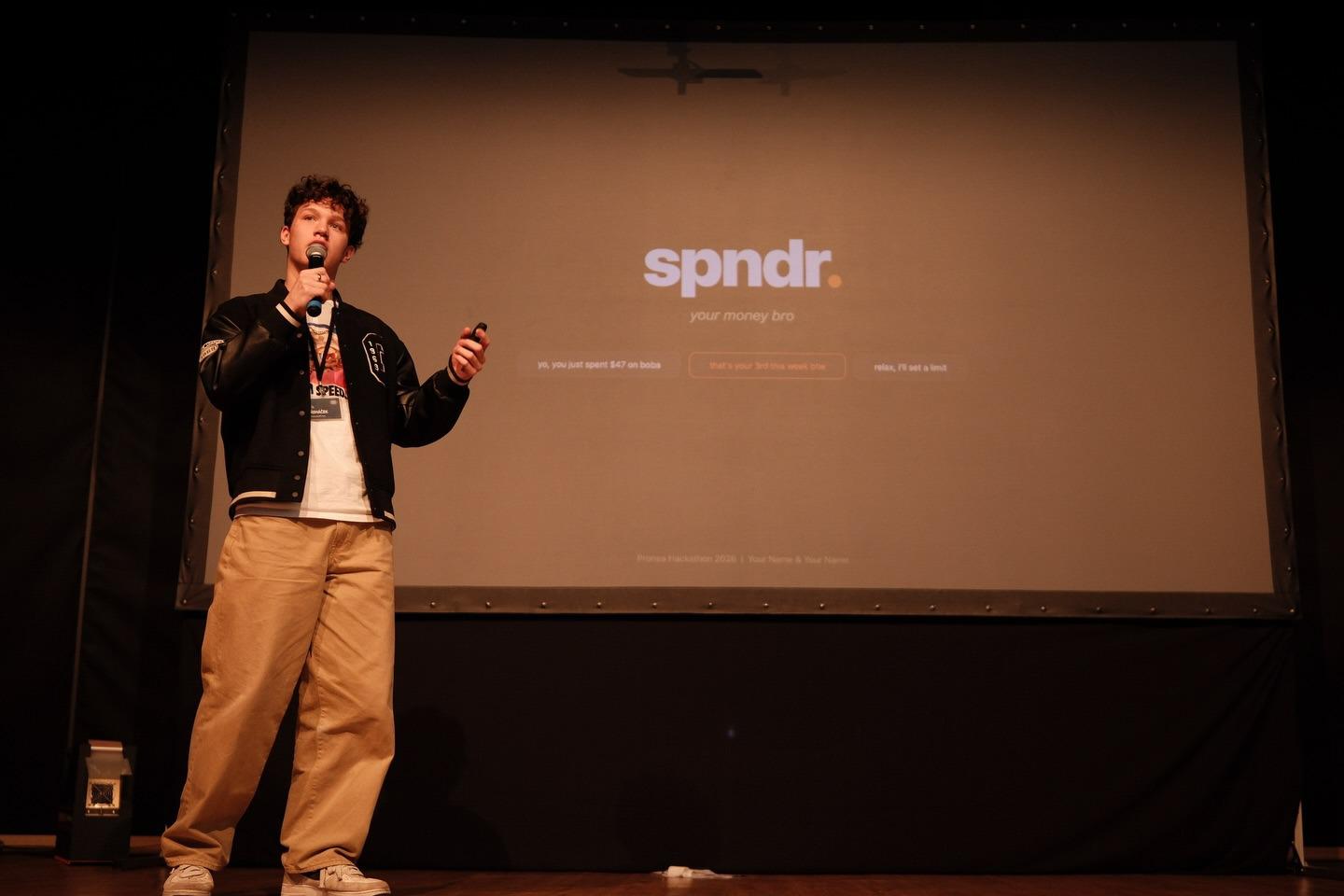 Pitching spndr on stage in front of the title slide at the Pronea Hackathon